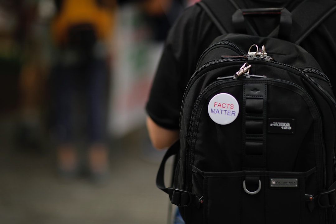 AI Facts - A white“Facts matter” pin on a black backpack on a person's back